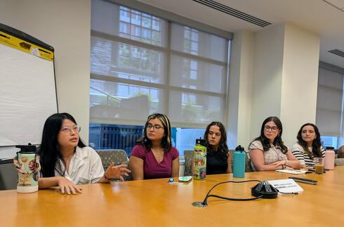 2024 BRIDGE intern cohort sit at a large conference table and discuss.