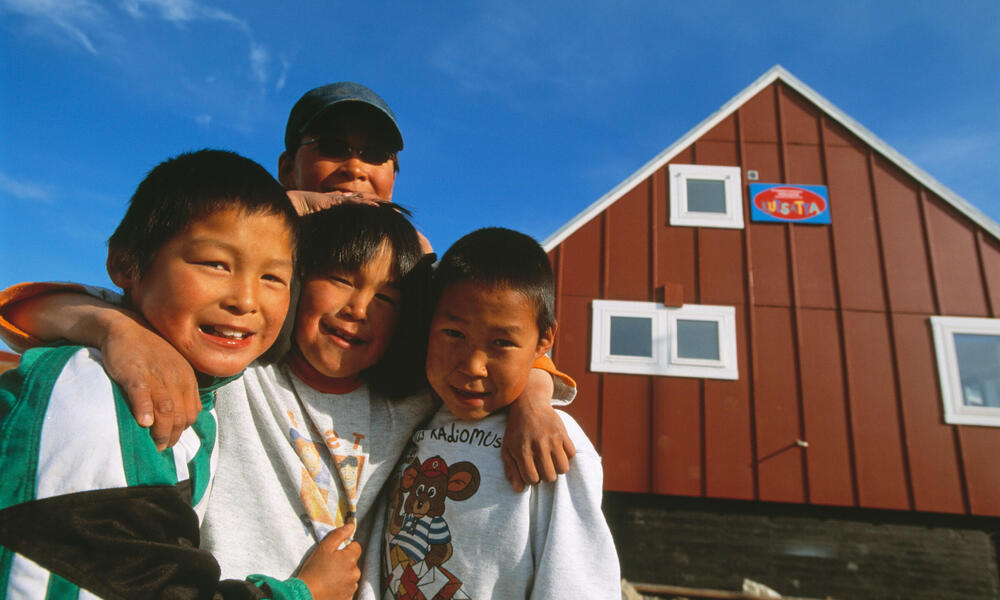 Inuit children smile in front of their home