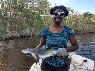 A Black woman smiling and holding a smalltooth shark for scientific research