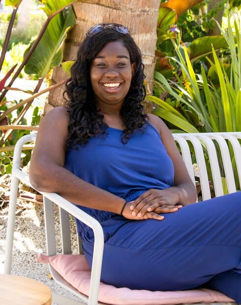 Jasmin Graham sitting in a chair and smiling. She is wearing a blue maxi dress.