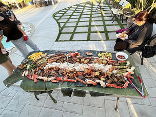 People gather around a large table covered with grilled banana leaves and food
