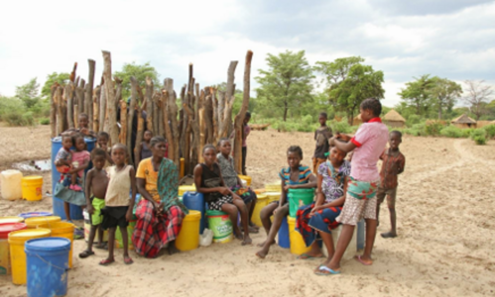 Members of the Kapau community sit on buckets used to transport water and look at the camera.