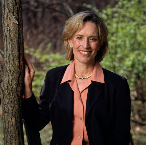 Kathryn Fuller wears a pink shirt and black blazer as she smiles at the camera next to a tree