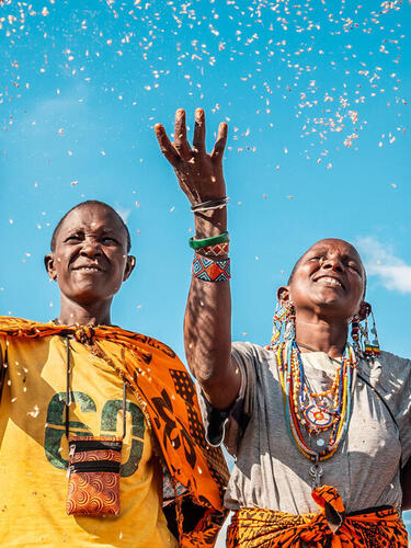 Four people in colorful clothing smiling and tossing seeds into the air