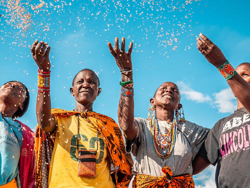 Four people in colorful clothing smiling and tossing seeds into the air