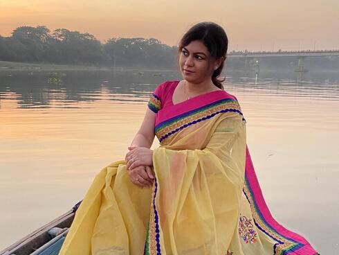 Portrait of Laila Sanjida sitting in a brightly colored gown along a river
