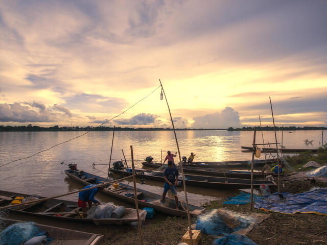 Fishermen outfit their long skinny boats with nets on the bank of a river at sunrise
