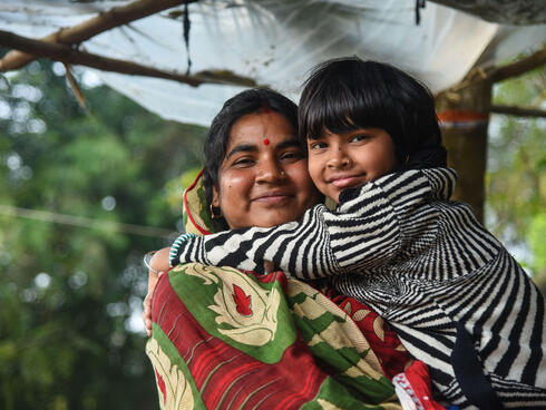 Mahua holds a child in a warm embrace and smiles at the camera