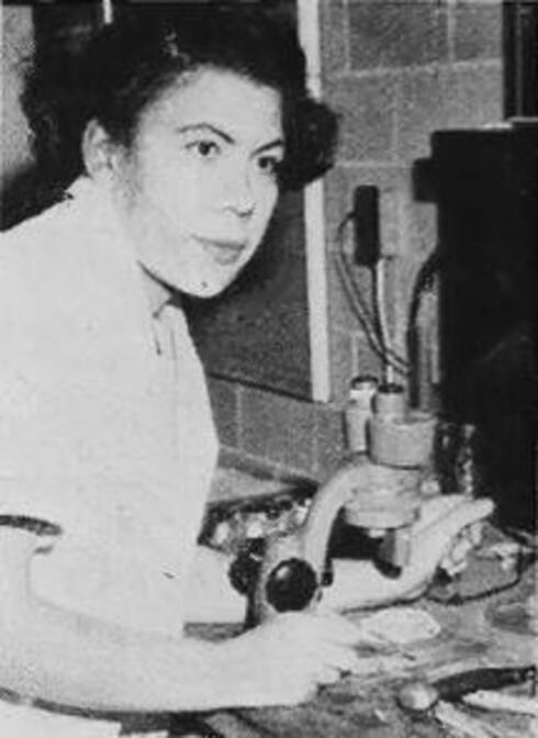 Margaret S. Collins stands in front of a microscope in a black and white photo