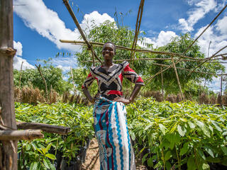 Mary Ngomapajo stands in a tree nursery on a sunny day