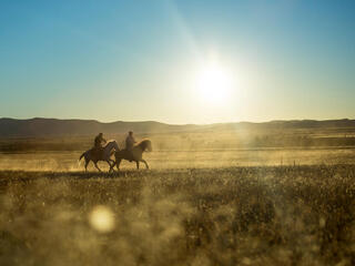 Father and son of ejido farm community ride their horses at sunset.