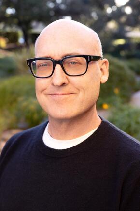 Headshot of Mike Mitchell, wearing black framed glasses and a black sweater