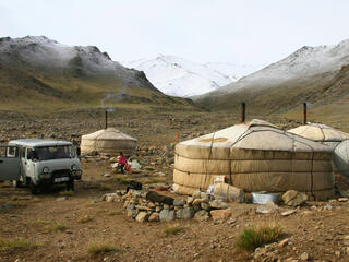 Three white covered yurt houses against a snowy mountain backdrop