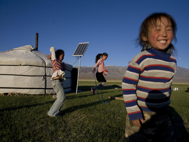 Children playing on the grass in front of their yurt home