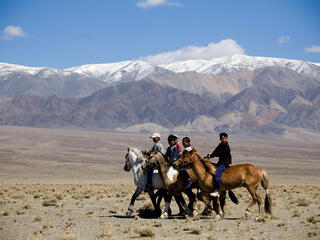 A group of children on horseback in a row in front of a large mountain range 