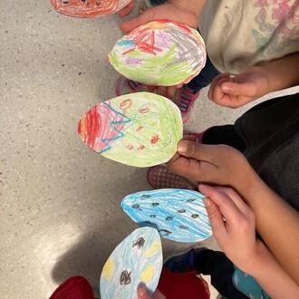 Children hold paper eggs that they decorated in many colors