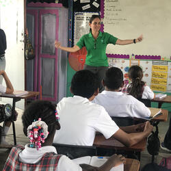 Nicole Auil Gomez stands at the front of a classroom with her arms outstretched