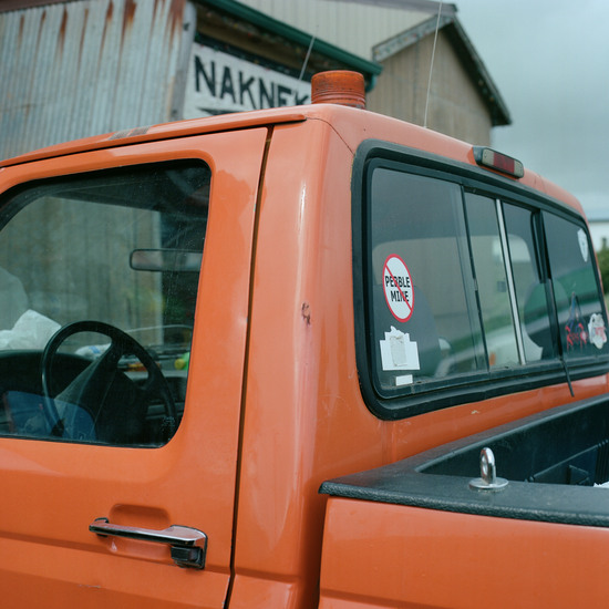 An orange pickup truck bears a sticker of the words 'Pebble Mine' with an x through them