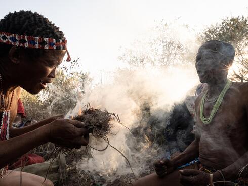 Two men of Nyae Nyae conservancy bend over sticks for traditional fire starting ceremony