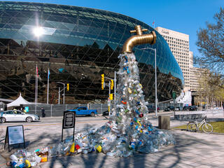 A sculpture of plastic bottles is shaped like a tap and stands in front of the building where negotiations on an international plastic treaty took place