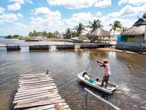 Man poling boat near shore with huts