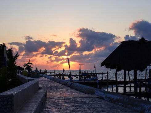 Sunset over ocean with silhouette of roofed docks