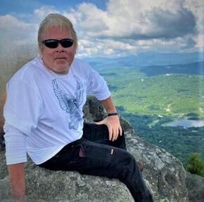 Patrick Browne sits on a rock in front of a mountain landscape