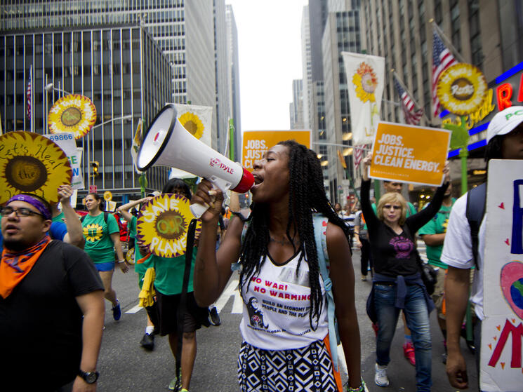 A lady with a megaphone, at the climate march, with other people marching with sunflower shaped signs
