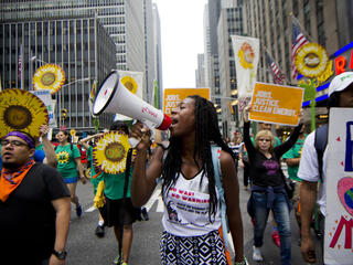 A lady with a megaphone, at the climate march, with other people marching with sunflower shaped signs