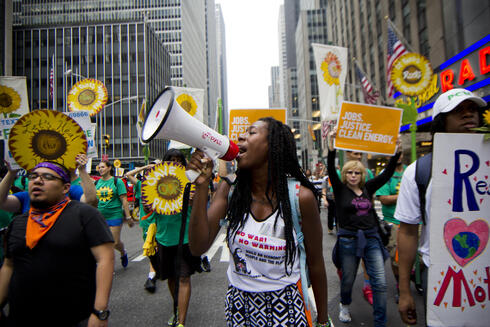 A lady with a megaphone, at the climate march, with other people marching with sunflower shaped signs