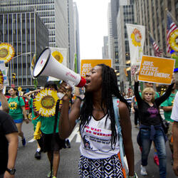 A lady with a megaphone, at the climate march, with other people marching with sunflower shaped signs