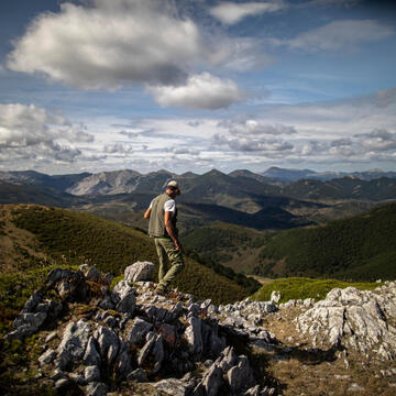 Shepherd walks over rocky ground overlooking beautiful landscape of hills and mountains in the distance