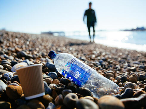 A man walks along the beach, next to an old plastic bottle and trash