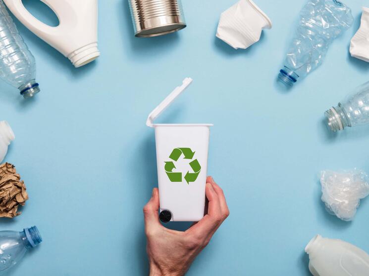 A semi circle of plastics surround a tiny recycling bin on a blue background