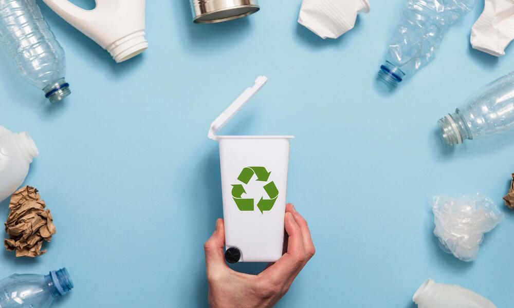 A semi circle of plastics surround a tiny recycling bin on a blue background