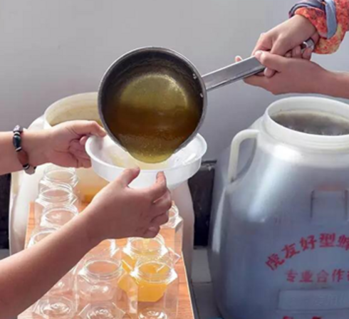 A large ladle pours honey into a big container