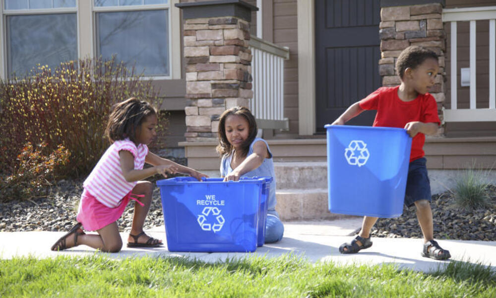 Children place items in recycling bins in front of a house