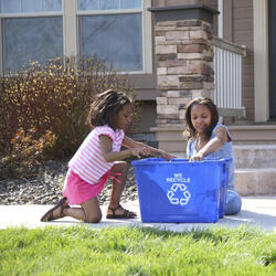 Children place items in recycling bins in front of a house