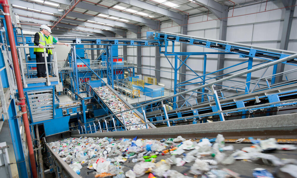 Two people stand on an elevated walkway overlooking a recycling plant