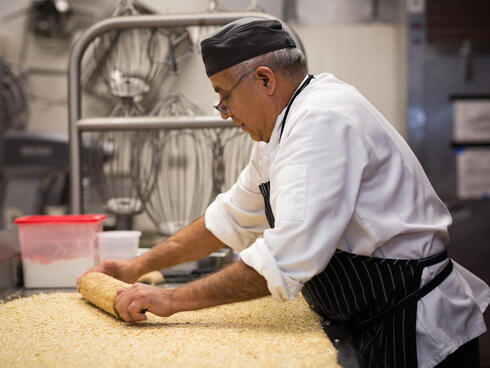 A chef rolls out dough on a counter in a hotel kitchen