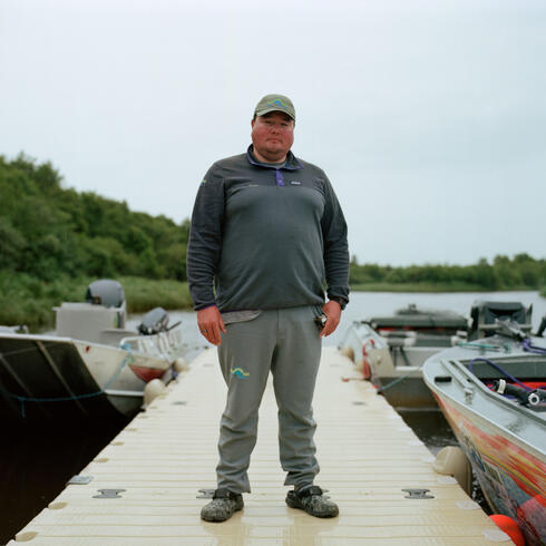 Reuben Hastings stands on a dock next to a motorboat and looks straight at the camera