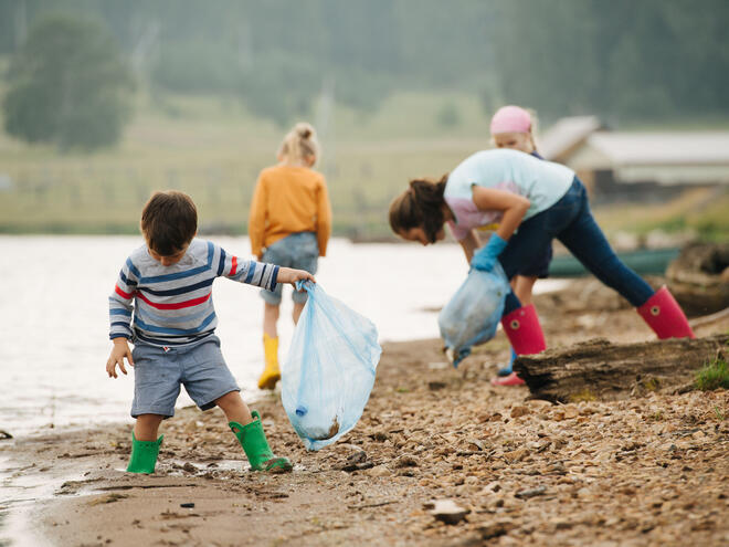 A group of people along a river bank clean up trash and put it in a trash back