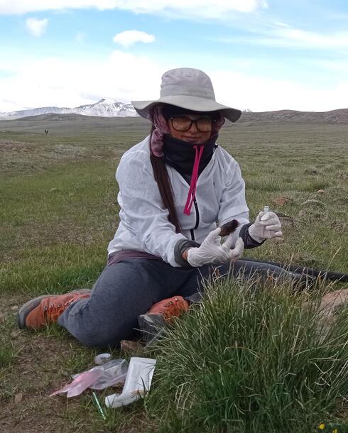 Sabita Gurung sits in a field holding a sample