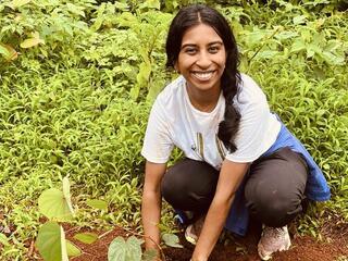 Sanjana Ramesh looks up at the camera while planting a plant in the soil
