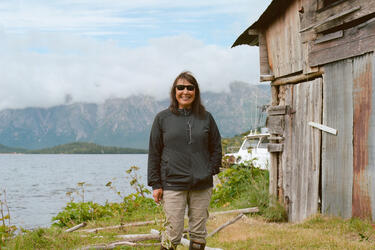 Sarah Thiele stands next to her smokehouse with a lake and mountains in the background