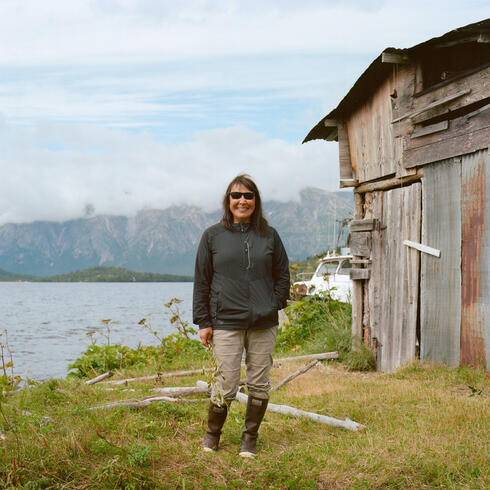 Sarah Thiele stands next to her smokehouse with a lake and mountains in the background