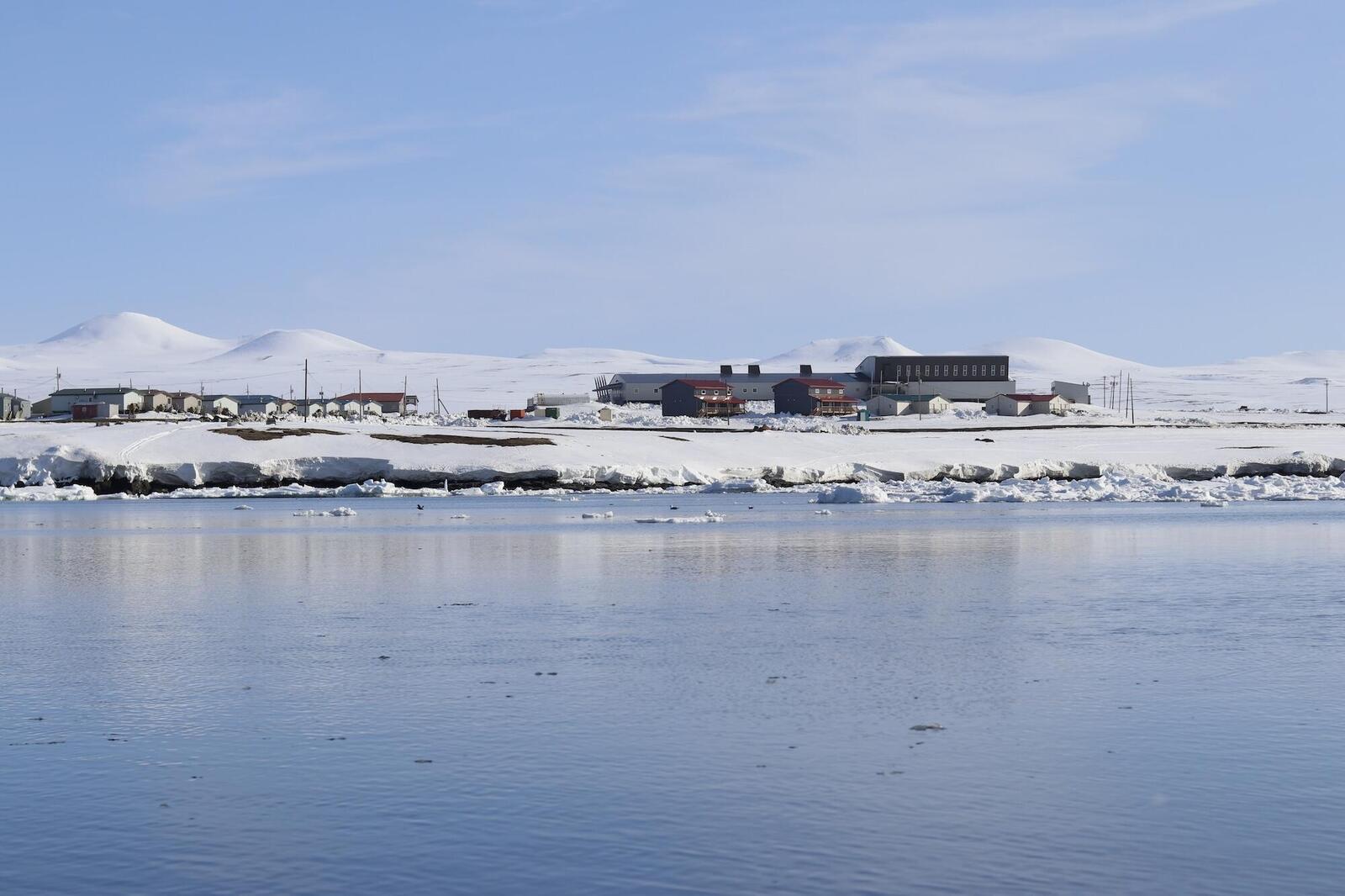 A snow land meets sea, with a few houses 