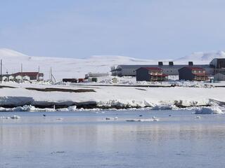 A snow land meets sea, with a few houses 