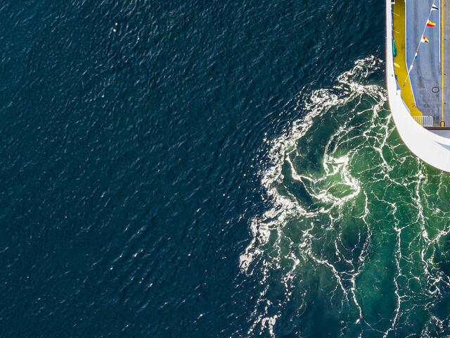 Aerial photo of ship on blue ocean with green swirls in wake