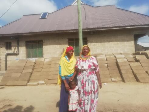 Sijali Kipuli with her daughter Alila and ground daughter Zulfak  in front of the latest house she has recently built  for 16,520USD 